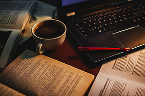 Cozy Study Desk Setup With Open Books, Coffee Cup, Red Pen, And Laptop Under Warm Lighting HD wallpaper