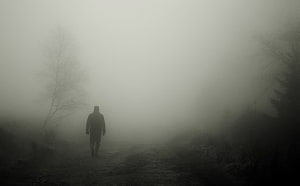 Solitary figure walking through dense fog on a desolate path HD wallpaper