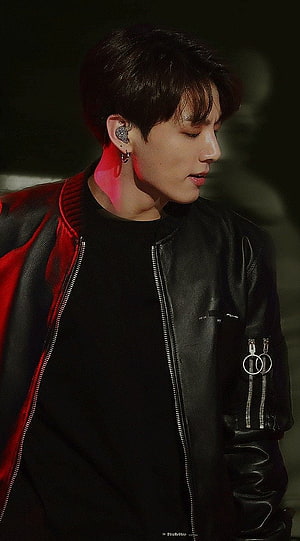 Jungkook from BTS in a black leather jacket with red accents and stage lighting HD phone wallpaper