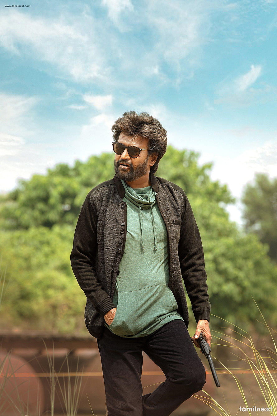 Rajinikanth in Petta holding a pistol outdoors with a green hoodie and dark cardigan HD phone wallpaper