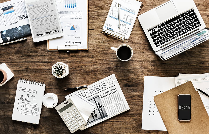 Top-down view of a cluttered office desk with laptop, calculator, business newspaper, and financial documents HD wallpaper