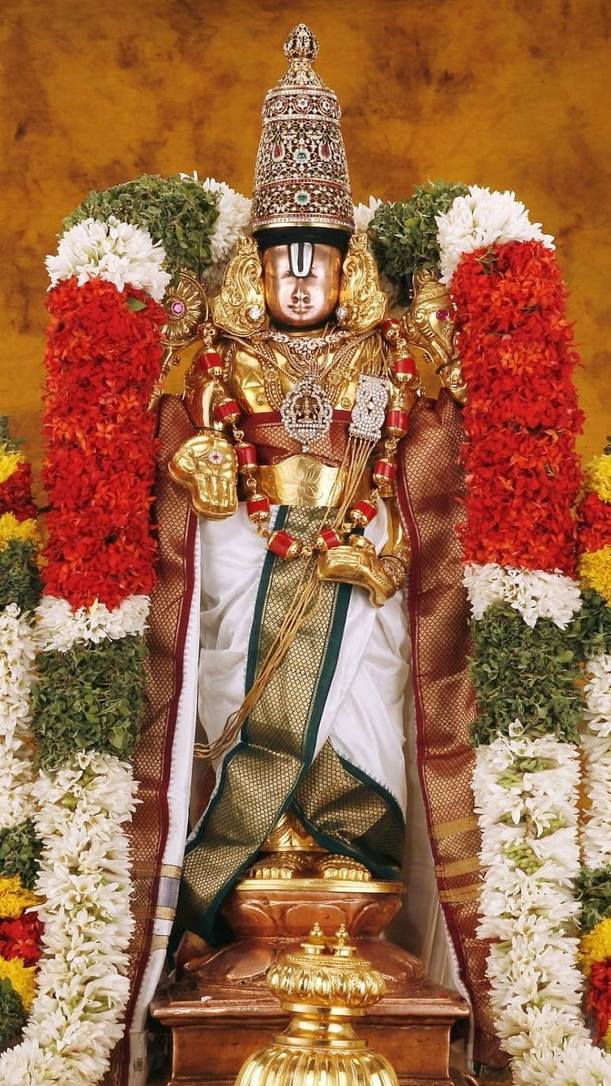 Ornate Balaji deity statue adorned with vibrant floral garlands and traditional gold jewelry HD phone wallpaper