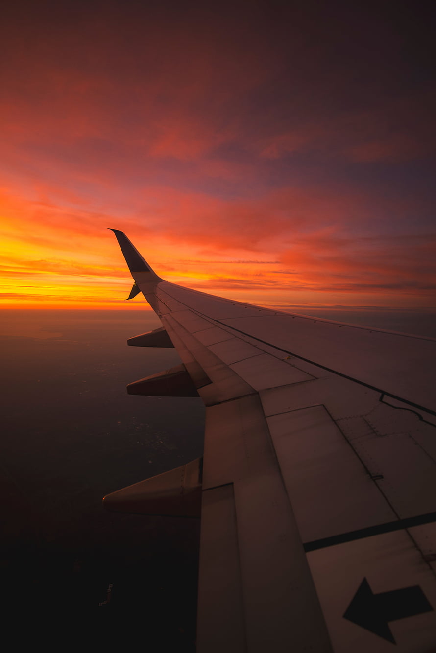 Airplane wing silhouette against a fiery orange and purple sunset sky from a passenger window view HD phone wallpaper