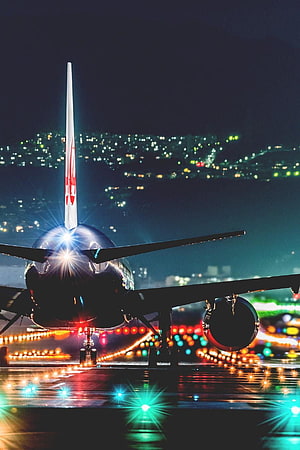 Commercial Jet Airliner On Wet Runway At Night With City Lights In Background HD phone wallpaper