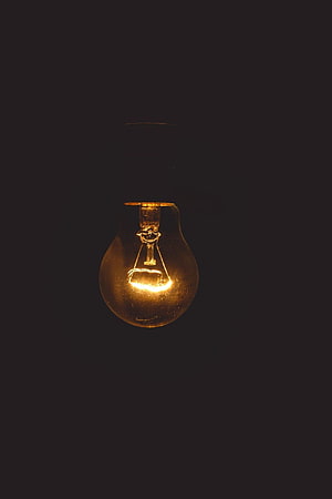 Glowing vintage incandescent light bulb suspended against a dark black background HD phone wallpaper