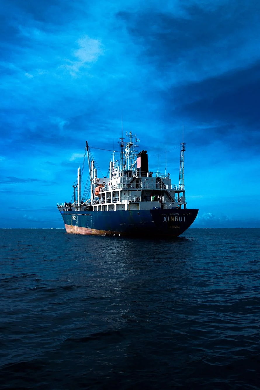 Cargo Ship Sailing on Deep Blue Ocean Under Dramatic Cloudy Sky HD phone wallpaper