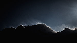 Dramatic Silhouette of Snow-Capped Mountain Peaks Under Dark Stormy Skies HD wallpaper