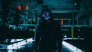 Anonymous figure in a glowing LED mask and dark hoodie standing in a neon-lit urban corridor at night HD wallpaper