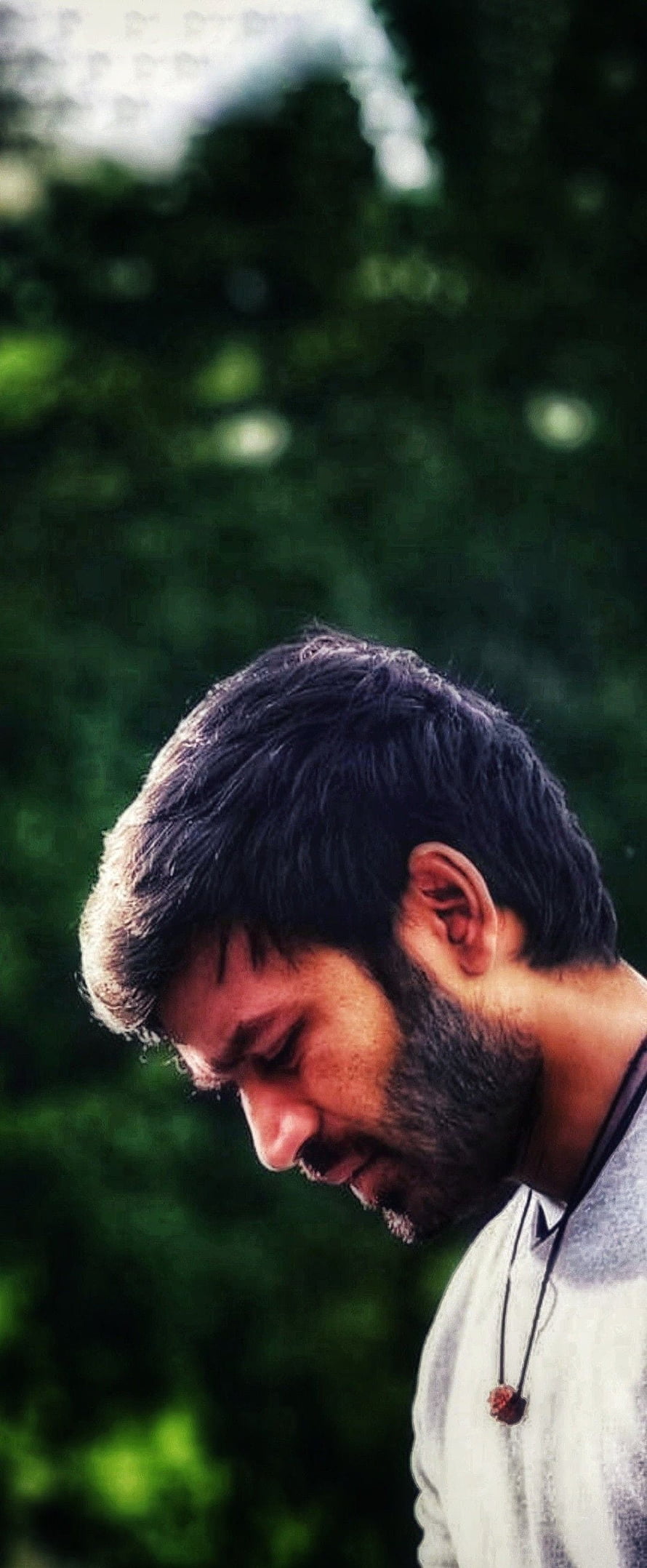 Dhanush in a contemplative profile portrait with a soft green bokeh background HD phone wallpaper