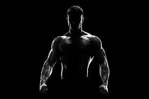 Dramatic Silhouette of a Muscular Male Athlete in a Dark Gym Setting HD wallpaper