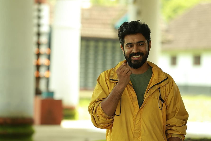 Nivin Pauly smiling in a yellow rain jacket with a warm outdoor backdrop HD wallpaper
