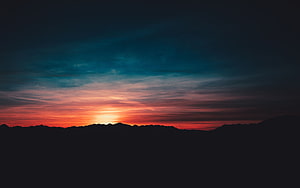 Dramatic Mountain Silhouette Against a Fiery Sunset Sky with Teal Clouds HD wallpaper