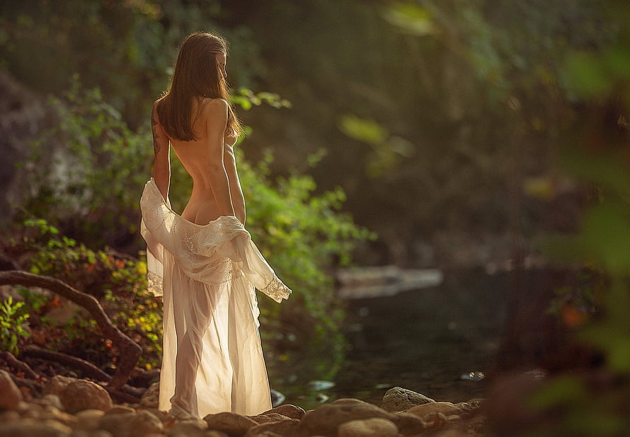 Ethereal Woman in Flowing White Dress Standing by a Forest Stream at Golden Hour HD wallpaper