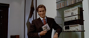 Patrick Bateman in a pinstripe suit holding a cassette tape in a modern room with audio equipment HD wallpaper