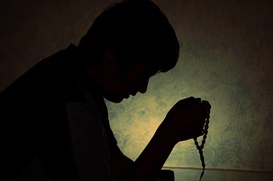 Silhouette of a man in quiet devotion holding prayer beads against a warm textured backdrop HD wallpaper