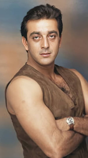 Sanjay Dutt in a rugged sleeveless brown shirt with arms crossed against a muted studio backdrop HD phone wallpaper