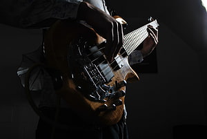 Close-up of a musician playing a wooden bass guitar in dramatic low-key lighting HD wallpaper