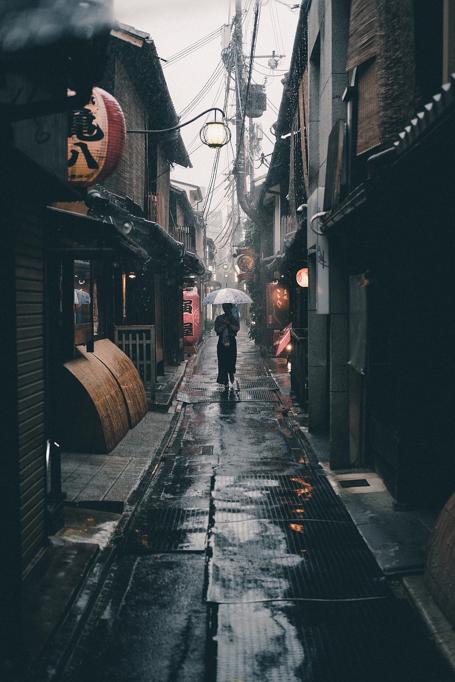 Solitary figure with umbrella walking through a narrow, rain-soaked traditional alley in Kyoto, Japan HD phone wallpaper