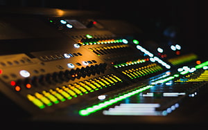 Professional Audio Mixing Console with Glowing Faders and Illuminated Level Meters in a Dark Studio HD wallpaper