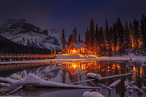 Illuminated Chalet Reflected in Frozen Lake at Winter Night with Snowy Mountains HD wallpaper