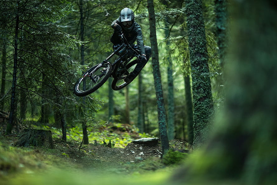 Mountain Biker Mid-Air Jump Through Dense Forest Trail HD wallpaper