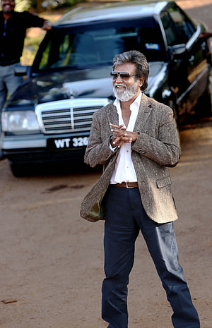 Rajinikanth in a brown blazer and sunglasses standing in front of a black Mercedes-Benz SUV HD phone wallpaper