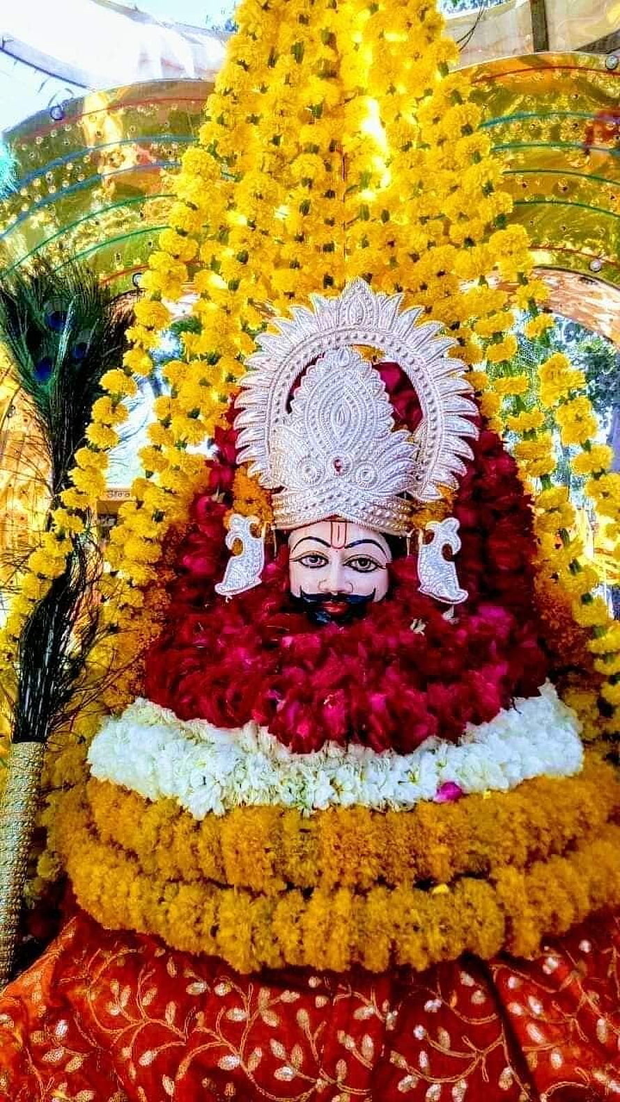 Lord Krishna adorned in vibrant marigold and rose garlands with ornate silver crown HD phone wallpaper