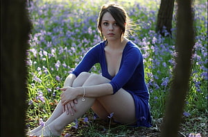 Young woman in a blue dress sitting barefoot in a field of purple wildflowers HD wallpaper