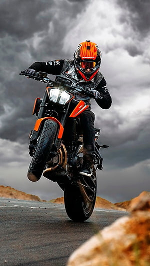 KTM Adventure Motorcycle Rider Performing a Wheelie on a Desert Road Under Stormy Skies HD phone wallpaper