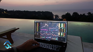 Laptop displaying stock market charts and trading data on a poolside deck at dusk HD wallpaper