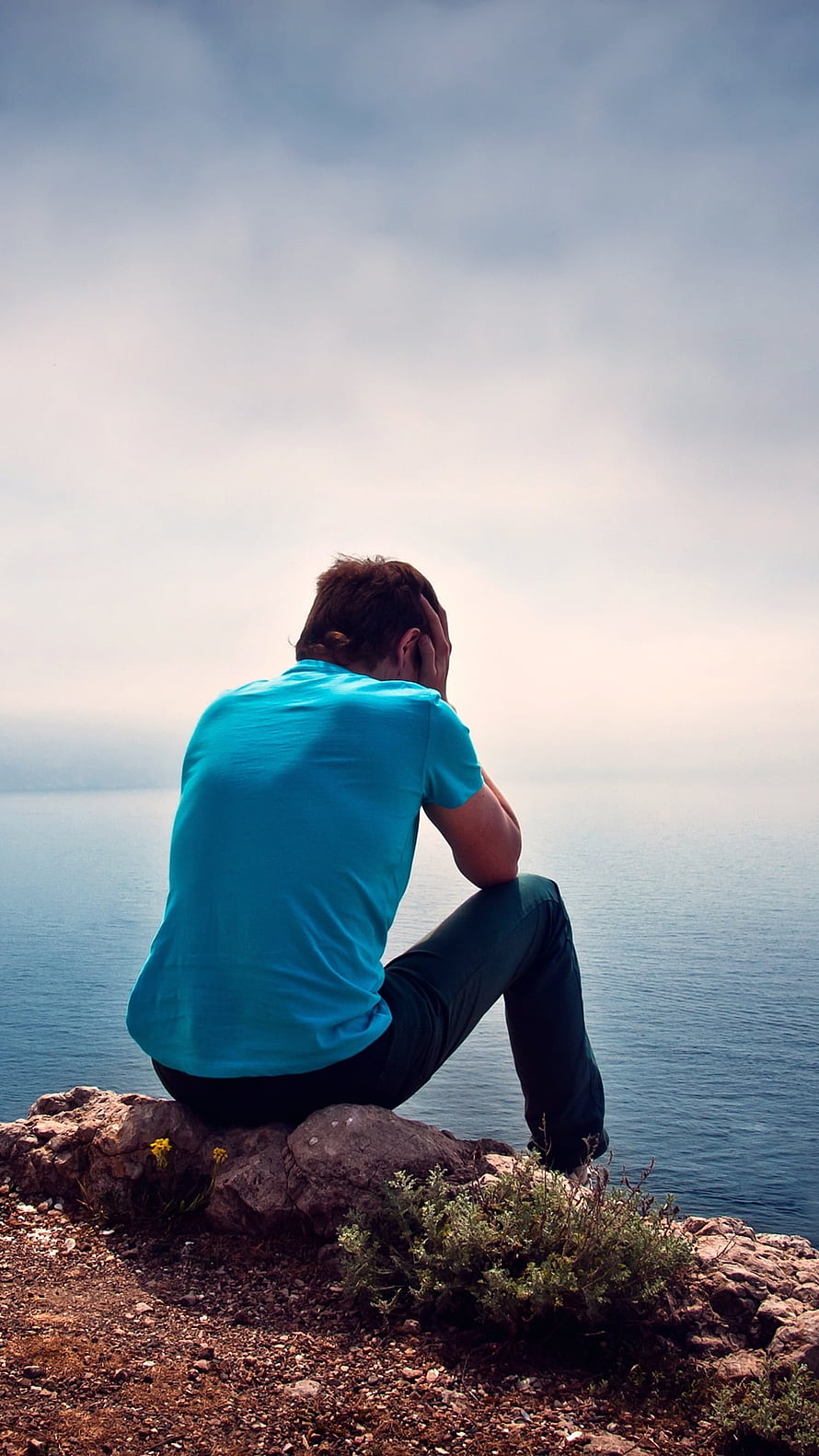 Man Sitting Alone on Rocky Cliff Overlooking the Sea in a Moment of Solitude HD phone wallpaper