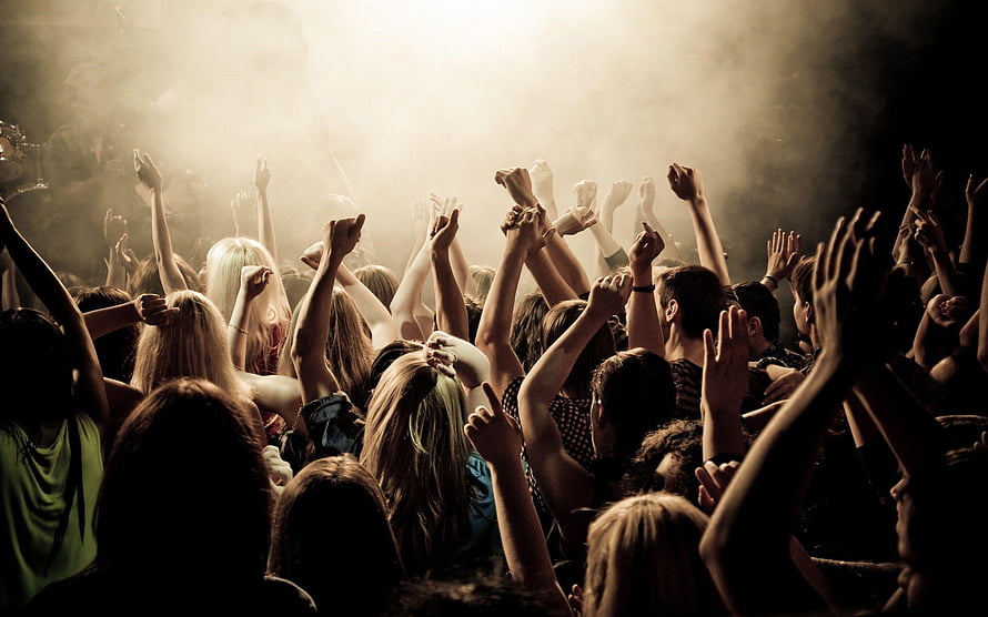 Energetic Concert Crowd With Raised Hands Under Warm Stage Lighting And Hazy Atmosphere HD wallpaper
