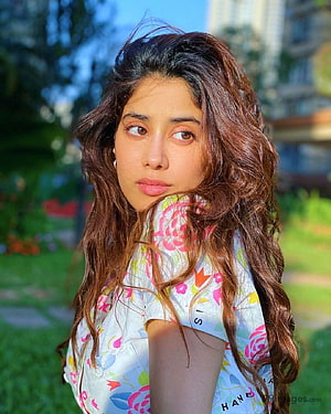 Janhvi Kapoor in a floral top with long wavy hair in a sunlit garden setting HD phone wallpaper