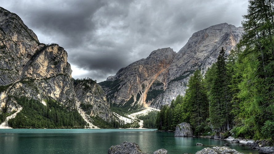 Dramatic Alpine Lake Landscape With Turquoise Water, Rocky Peaks, And Dense Evergreen Forest Under Stormy Skies HD wallpaper