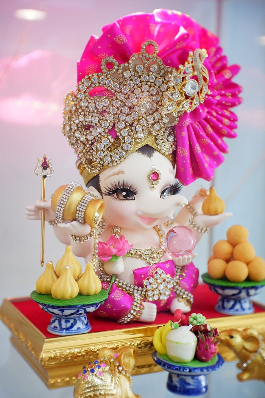 Adorned Baby Ganesha Idol With Pink Headdress, Gold Jewelry, And Traditional Offerings HD phone wallpaper