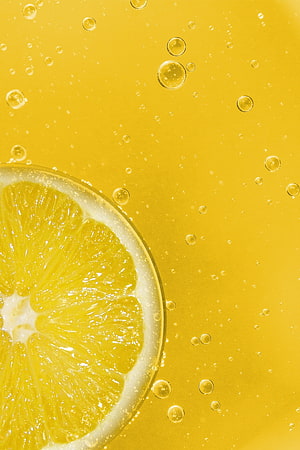 Fresh lemon slice submerged in golden sparkling liquid with rising carbonation bubbles HD phone wallpaper
