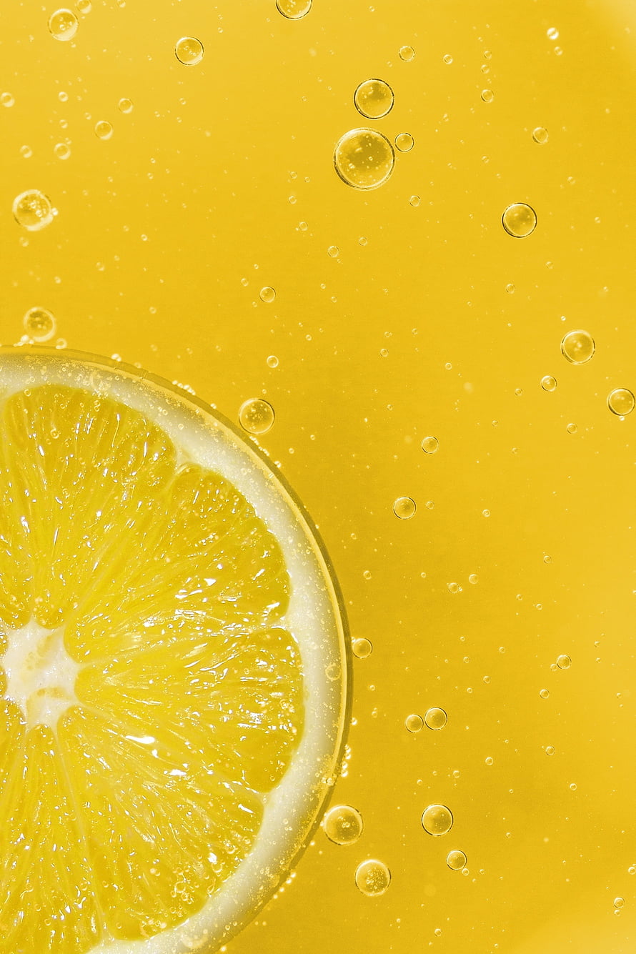 Fresh lemon slice submerged in golden sparkling liquid with rising carbonation bubbles HD phone wallpaper