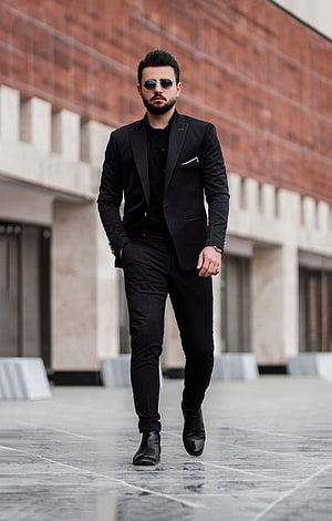 Man in all-black tailored suit and sunglasses walking on a city plaza HD phone wallpaper