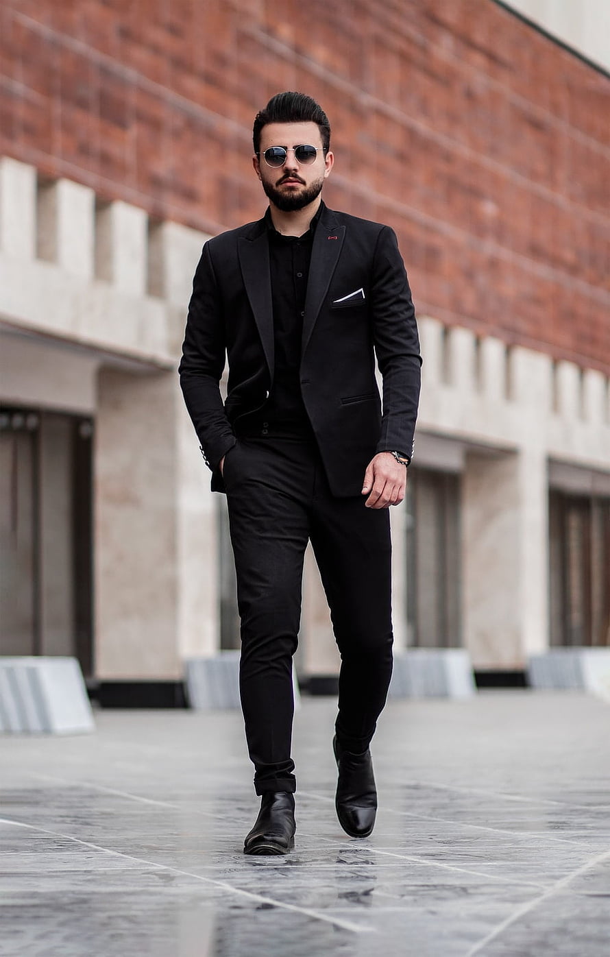 Man in all-black tailored suit and sunglasses walking on a city plaza HD phone wallpaper