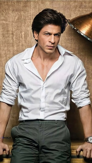 Shah Rukh Khan in a white shirt and dark trousers against a textured brown backdrop HD phone wallpaper