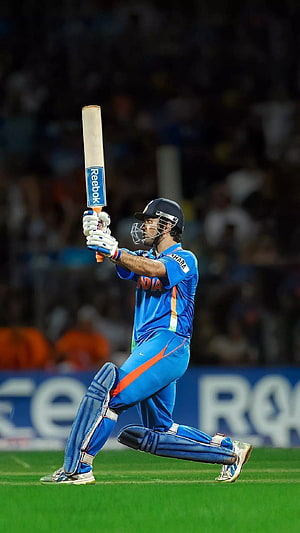 MS Dhoni in Indian cricket blue kit mid-swing with Reebok bat on a floodlit stadium pitch HD phone wallpaper
