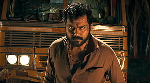 Karthi as an escaped prisoner in Kaithi standing before a yellow bus at night HD wallpaper