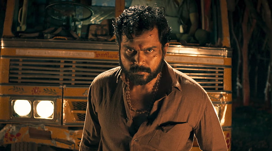 Karthi as an escaped prisoner in Kaithi standing before a yellow bus at night HD wallpaper