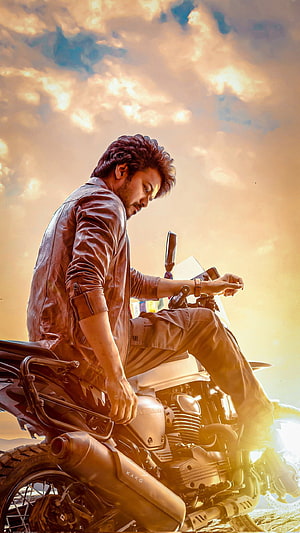 Thalapathy Vijay on a Royal Enfield motorcycle against a dramatic golden sunset sky HD phone wallpaper