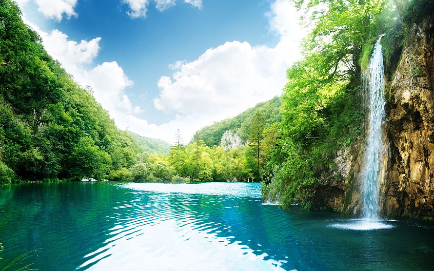 Serene turquoise lake with a cascading waterfall surrounded by lush green forest and rocky cliffs HD wallpaper