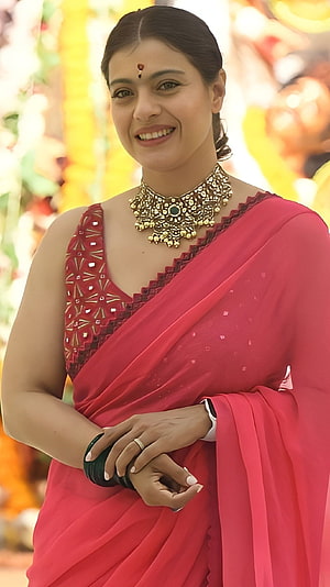 Kajol in a vibrant pink saree with traditional gold jewelry and festive backdrop HD phone wallpaper