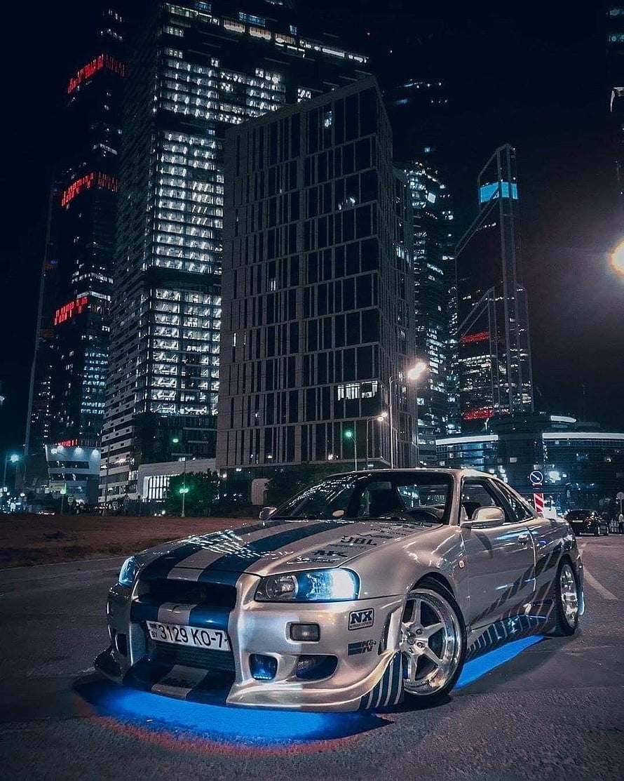Silver Nissan Skyline GT-R R34 with Blue Underglow Parked in a City at Night HD phone wallpaper
