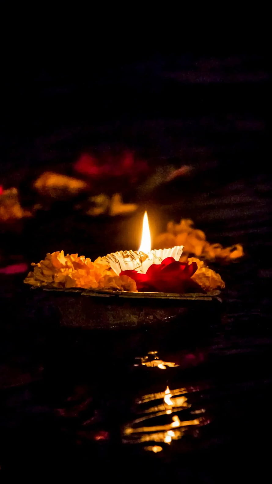 Glowing Diya with Marigold Flowers and Red Rose Floating on Water at Night HD phone wallpaper