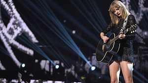 Taylor Swift performing live on stage with an acoustic guitar under dramatic blue spotlights HD wallpaper