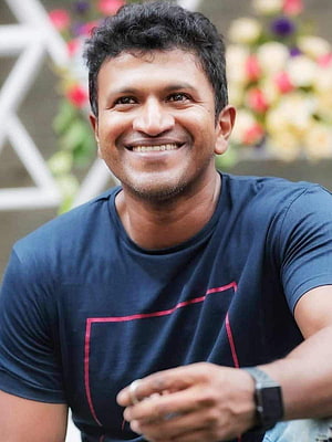 Puneeth Rajkumar smiling portrait in navy t-shirt with floral background HD phone wallpaper
